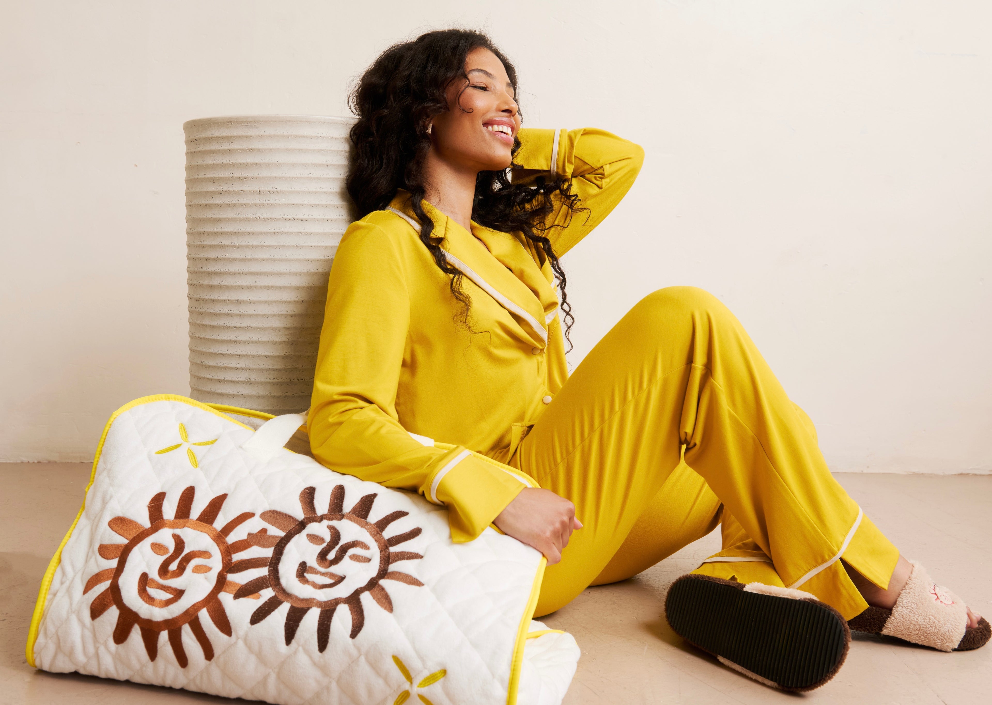 Woman in yellow pajamas sitting on the floor with a decorative pillow. Responsible fashion brand